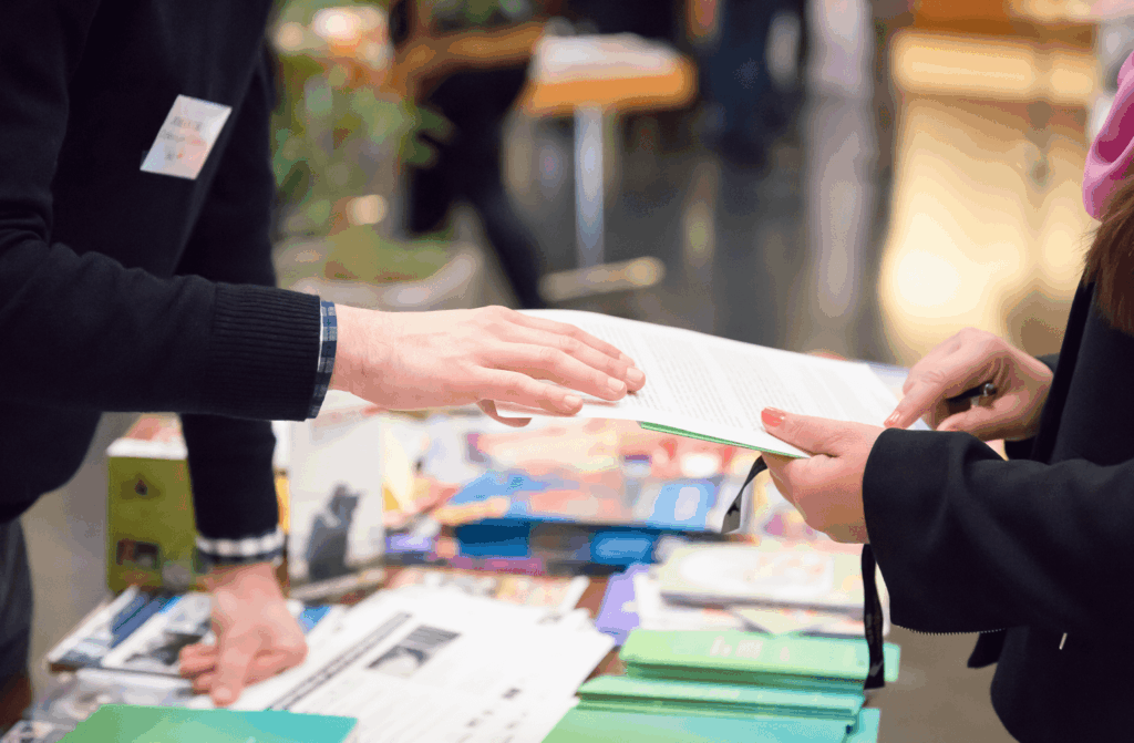 Two people having a conversation at an education exhibition, exchanging documents
